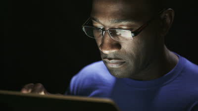 stock-footage-close-up-of-young-black-man-reading-his-tablet-in-the-dark-black-background